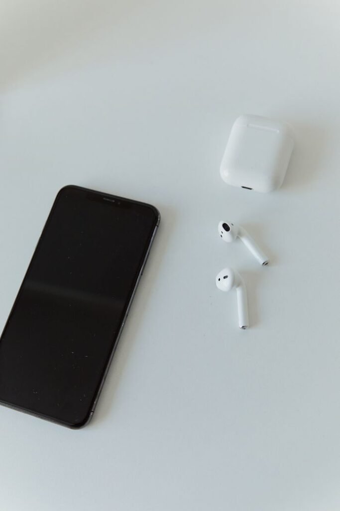 A modern smartphone and wireless earphones on a minimalist white table, embodying contemporary technology.